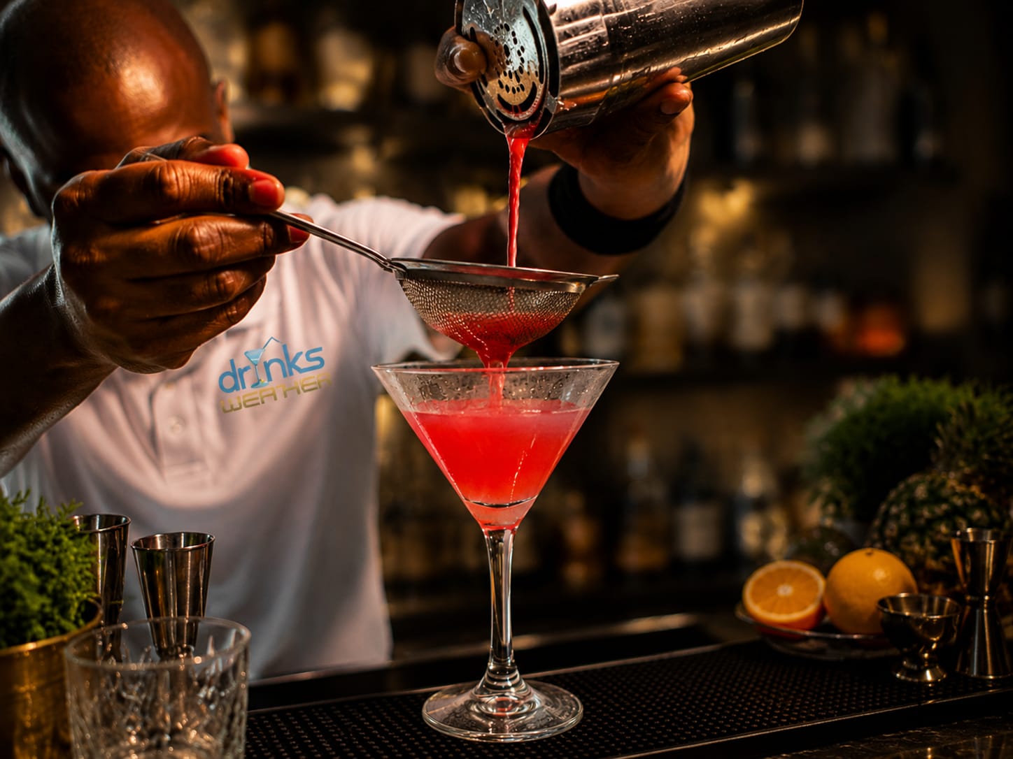 Bartender pouring a red cocktail into a martini glass